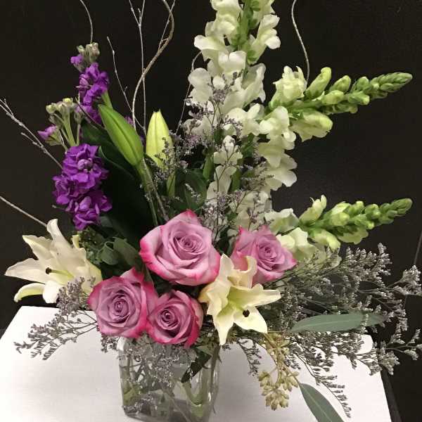 Mixed bouquet of pink roses, white lilies, and purple snapdragons in a glass vase