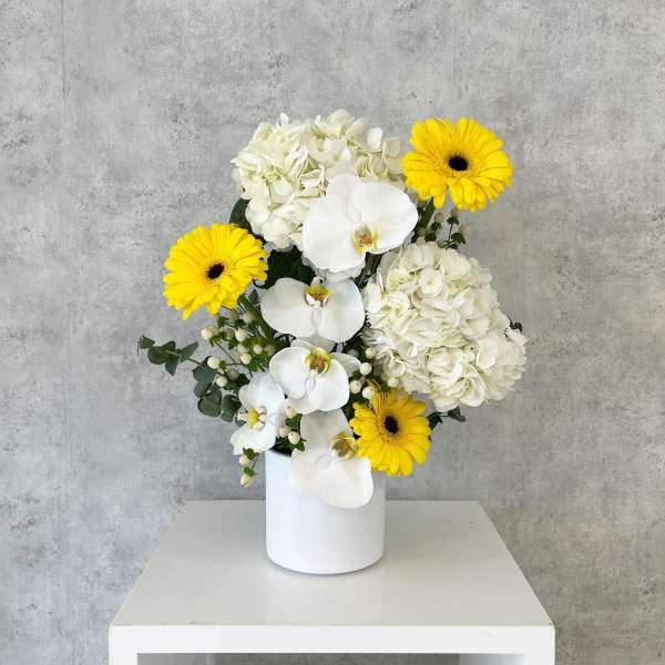 White orchids, hydrangeas, and yellow gerbera daisies in a white vase