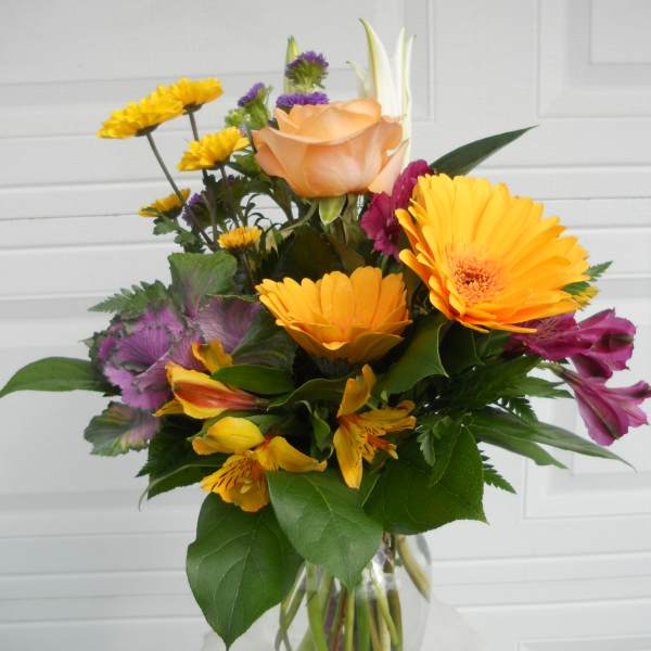 Mixed bouquet in a clear glass vase with orange, yellow, and purple flowers