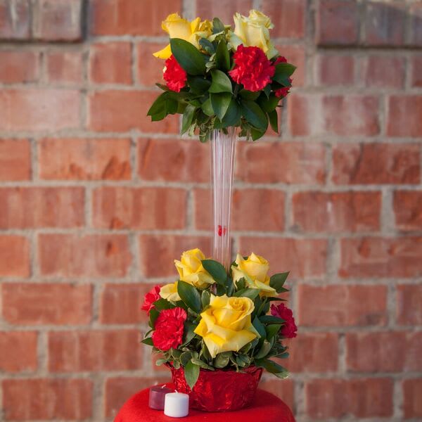 Two-tier floral arrangement with yellow roses and red carnations in a clear stand