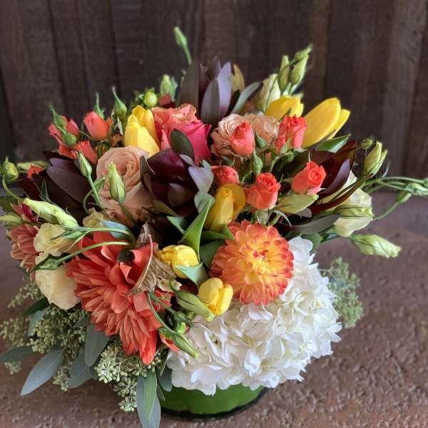 Colorful mixed bouquet with roses, tulips, dahlias, and hydrangea in a green vase