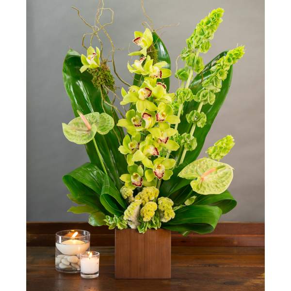 Green orchid arrangement in a wooden box with two candles nearby