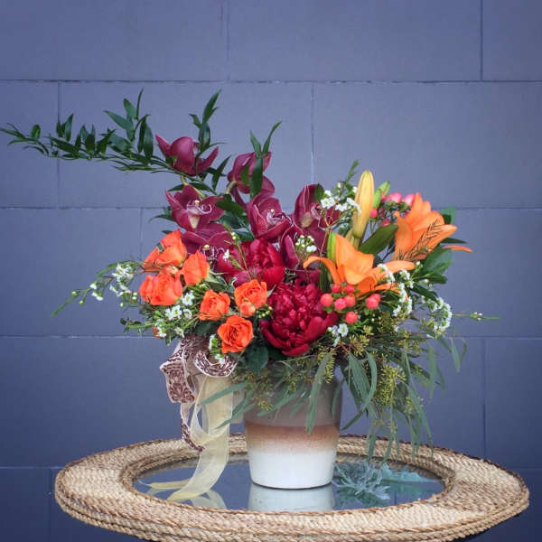 Mixed bouquet with orange lilies, red orchids, and orange roses in a ceramic vase