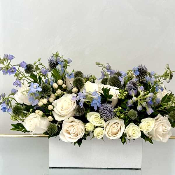 White roses and blue flowers arranged in a white box