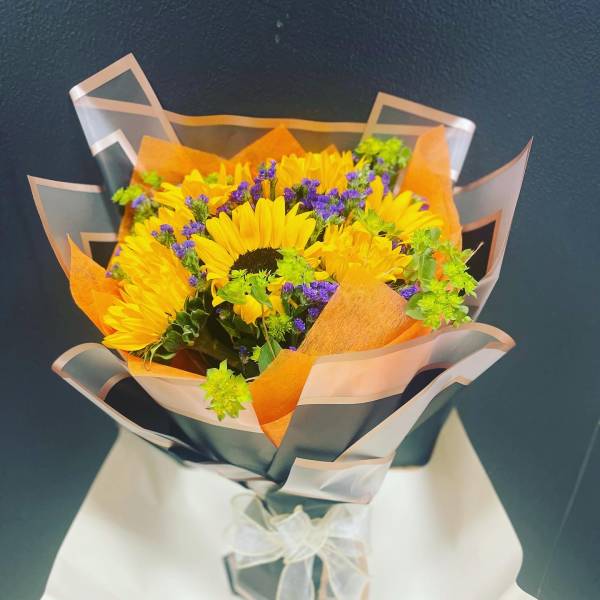 Bouquet of yellow sunflowers with purple filler flowers wrapped in orange and clear paper