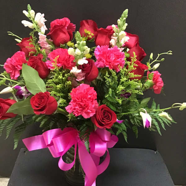 Red roses and pink carnations in a vase with a pink ribbon