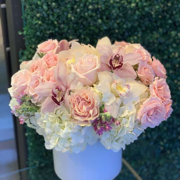 Pink roses and orchids arranged in a white hat box