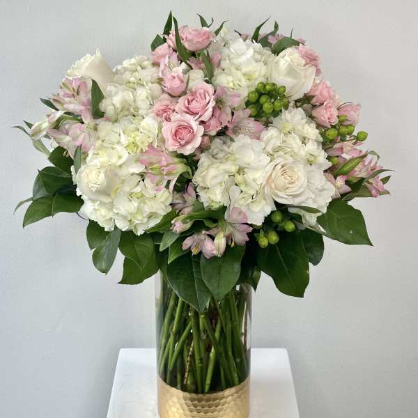 Pink and white bouquet in a clear glass vase with a gold base