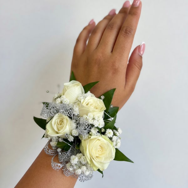White rose wrist corsage with baby's breath and silver ribbon on a hand