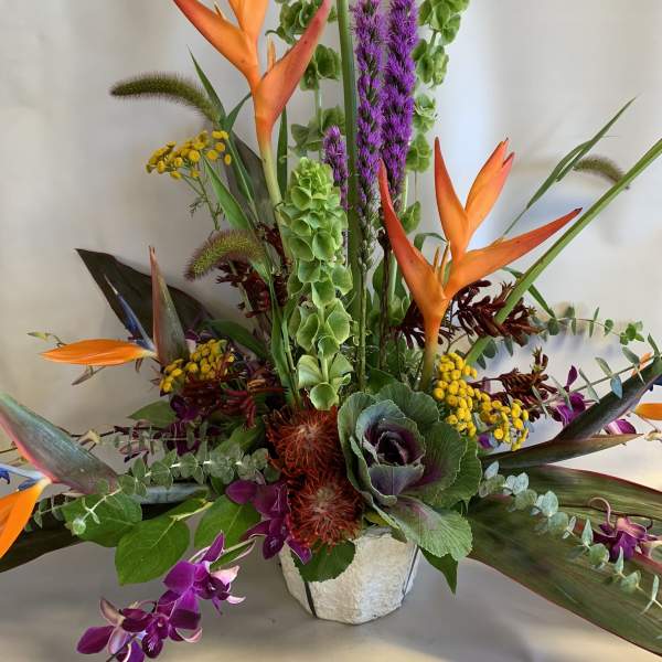 Tropical arrangement with orange bird-of-paradise and purple orchids in a white vase