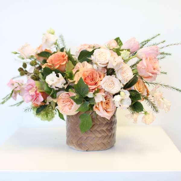 Peach and white rose bouquet in a woven basket vase