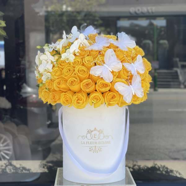 Yellow roses in a white hatbox with white orchids and butterfly decorations