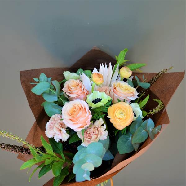 Bouquet of peach and yellow roses with eucalyptus in brown paper