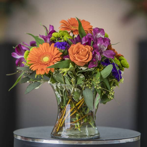 Mixed bouquet of orange, purple, and green flowers in a clear glass vase