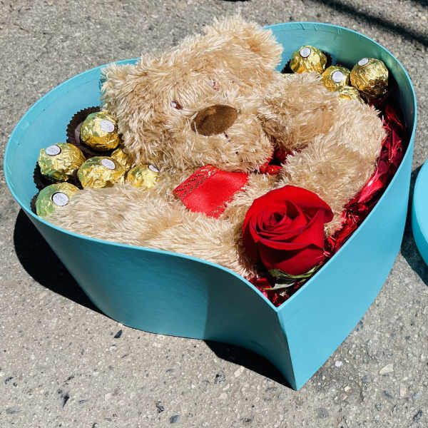 Teddy bear and chocolates in a turquoise heart-shaped box with a red rose