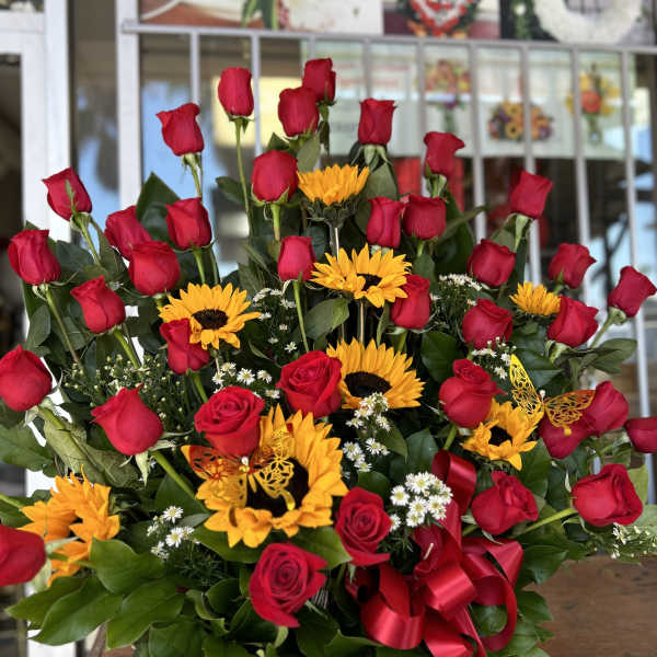 Basket arrangement of red roses and yellow sunflowers with a red ribbon