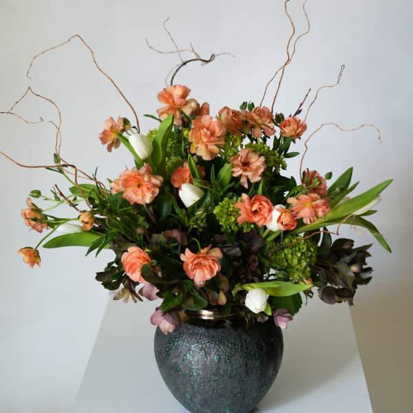 Peach and white flowers arranged in a dark vase with curly branches
