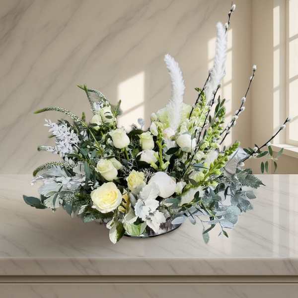 White rose arrangement with tall feather accents in a low bowl