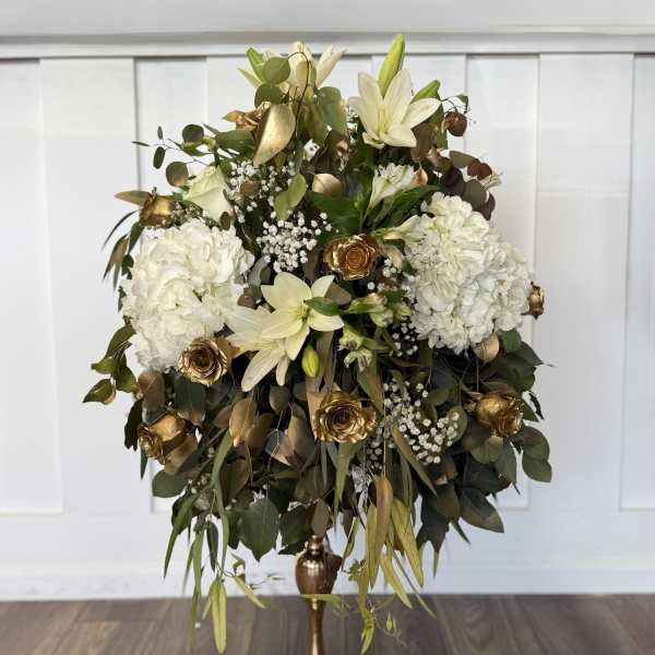 White floral arrangement with gold roses in a tall gold vase