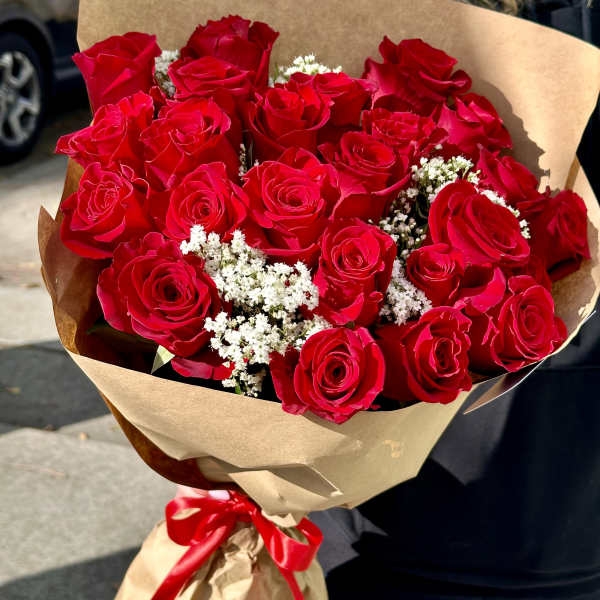 Large bouquet of red roses with white filler flowers wrapped in brown paper and a red ribbon
