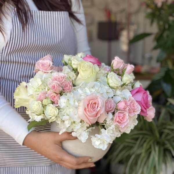 Pink and white roses arranged in a white bowl vase