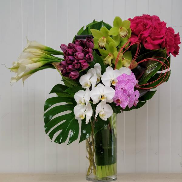 Mixed bouquet with orchids, roses, calla lilies, and tulips in a glass vase