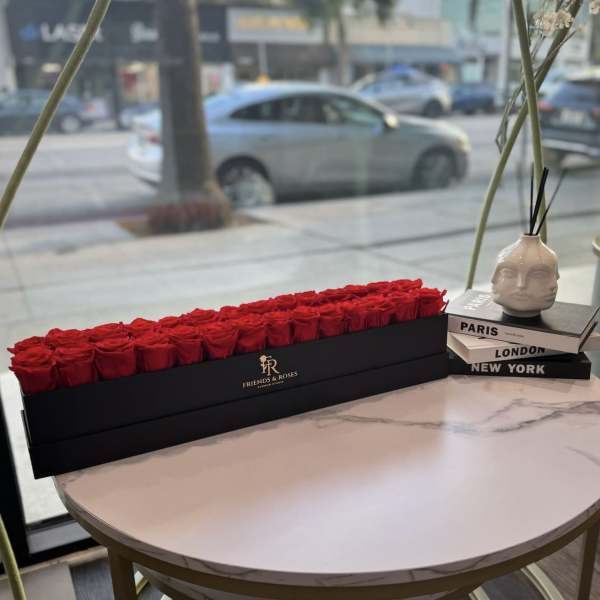 Long black box filled with red roses on a round table