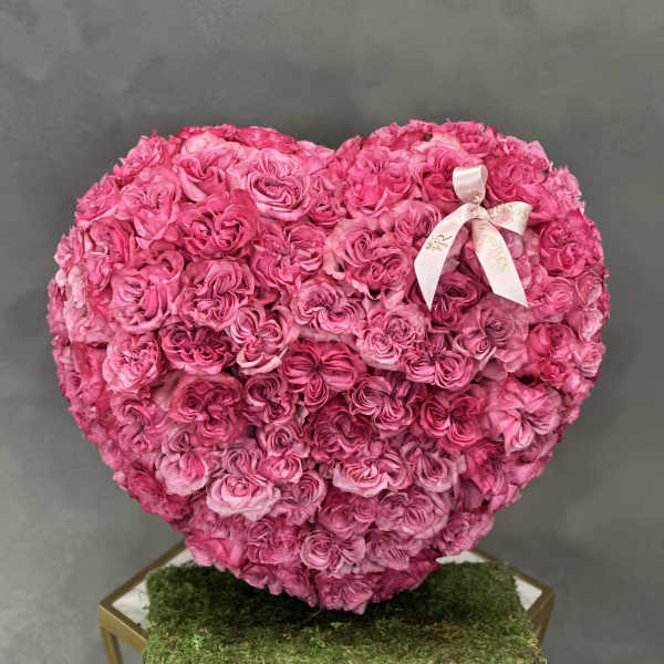 Heart-shaped arrangement of pink roses with a ribbon on a moss-covered base