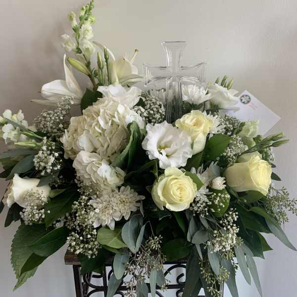 White floral arrangement with roses, lilies, and a clear glass cross