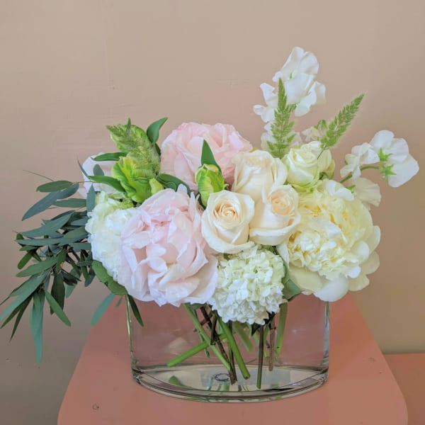 Pastel bouquet of roses, hydrangea, and white blooms in a clear glass vase