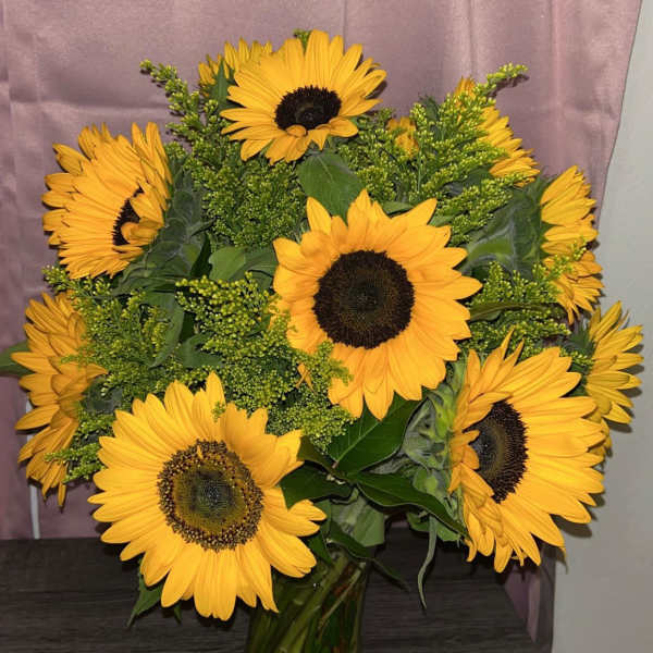 Bouquet of large yellow sunflowers in a clear glass vase on a dark wood surface