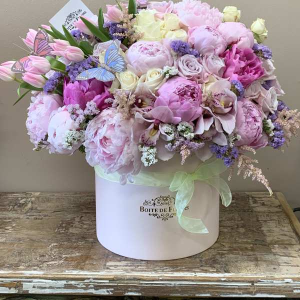 Pink and white floral arrangement in a round box with butterfly picks