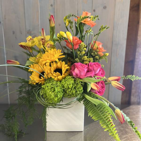 Bright mixed bouquet in a white square vase with sunflowers and pink roses