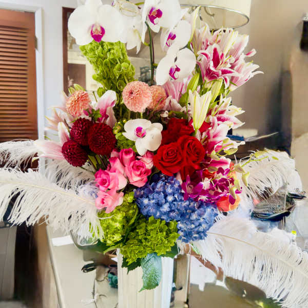 Colorful bouquet with orchids, roses, lilies, hydrangeas, and feathers in a white vase