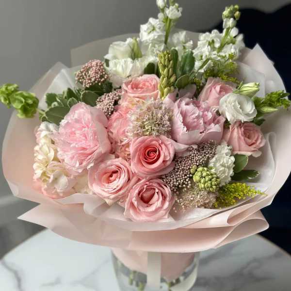 Pink and white bouquet of roses and mixed blooms wrapped in pale paper