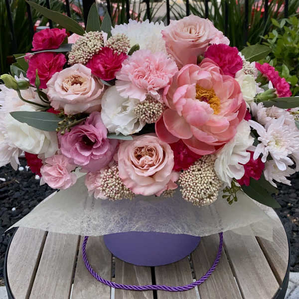Pink and white mixed bouquet with roses, peonies, and carnations in a purple box