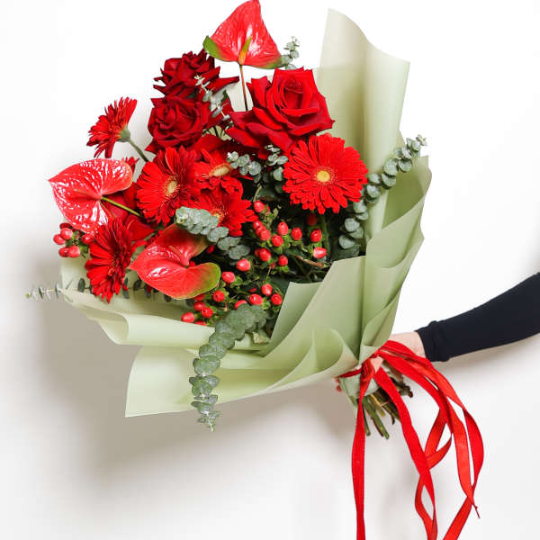 Bouquet of red roses and gerbera daisies wrapped in pale green paper