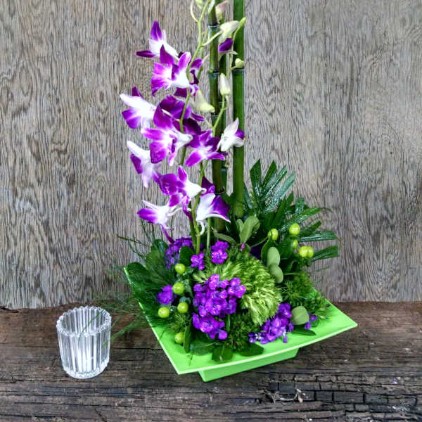 Purple orchids in a green square vase with a small glass candle holder