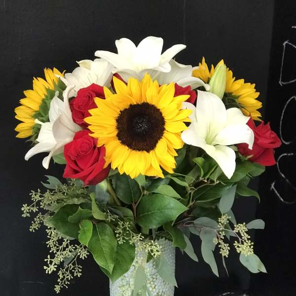 Bouquet of sunflowers, white lilies, and red roses in a textured vase