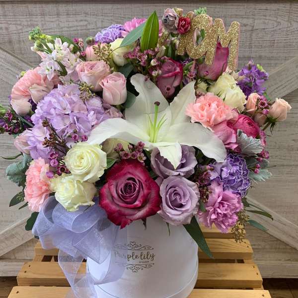 Pastel bouquet of roses, lilies, and carnations in a white hat box with a glittery "M" topper