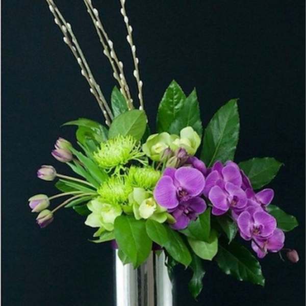 Purple orchids and green flowers in a tall silver vase