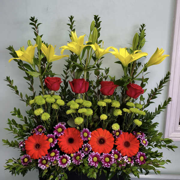 Tall mixed flower arrangement with yellow lilies, red roses, and bright daisies