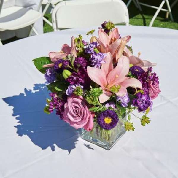 Pink and purple floral centerpiece in a square glass vase