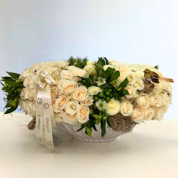 Cream rose arrangement in a white bowl with ribbon and bird accents