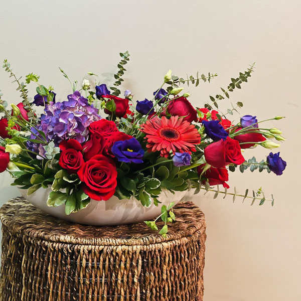 Mixed bouquet of red roses, purple blooms, and a pink gerbera daisy in a white bowl