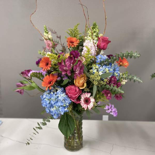 Mixed bouquet in a glass vase with bright orange, pink, blue, and purple flowers