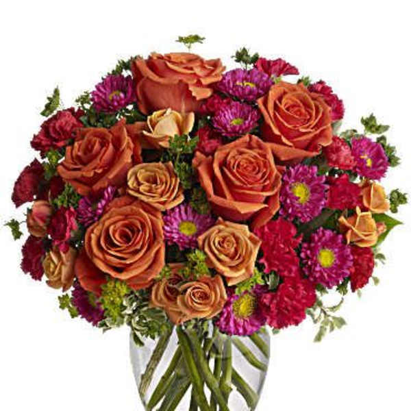 Orange roses and magenta daisies in a clear glass vase