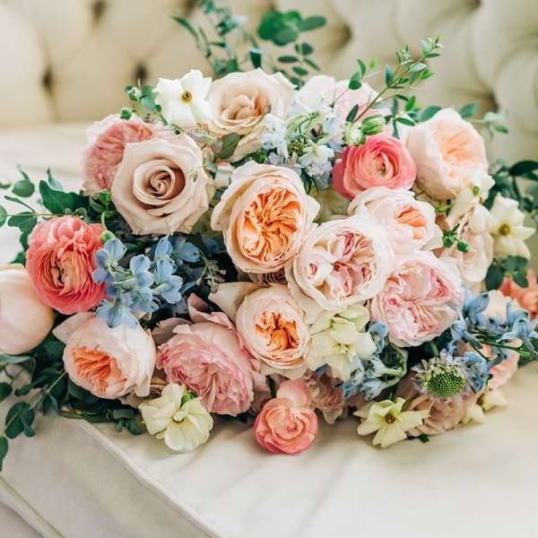 Bouquet of blush and peach roses with blue flowers on a cream sofa