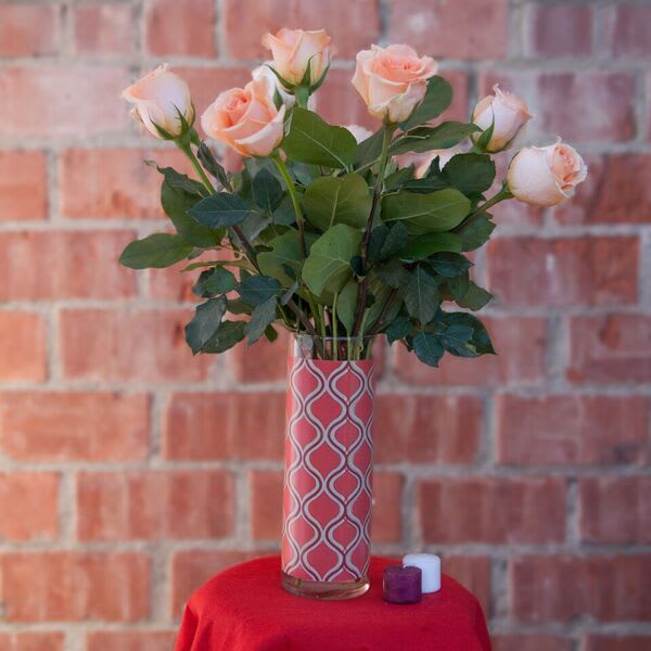 Peach roses in a patterned glass vase with two small candles