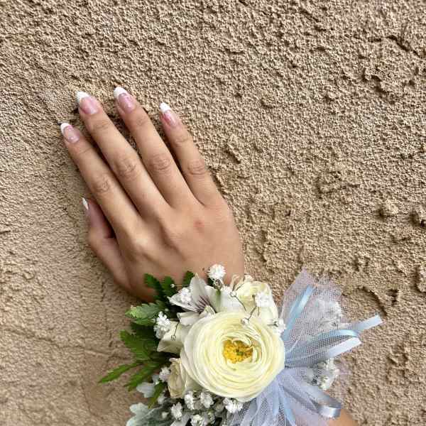 White floral wrist corsage with blue ribbon on a hand